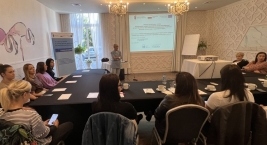 Grupa ludzi siedzi przy stole w jasnym pomieszczeniu, prowadząc rozmowę