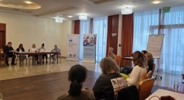 Uczestnicy słuchają prowadzącej; roll-upy projektu w tle