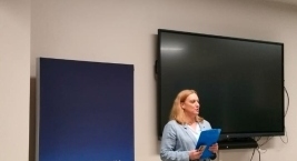 Prezentacja kobiety dla grupy osób w sali, wszyscy skupieni na mówcy