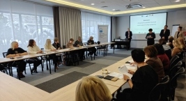 Ludzie siedzący przy stołach w sali, zaangażowani w rozmowy i wymianę myśli.