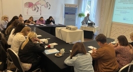 W pokoju siedzi grupa osób przy stole, zapisują coś na kartkach