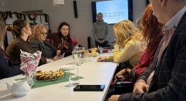 Pani prowadząca stoi i przedstawia, a uczestnicy siedzą