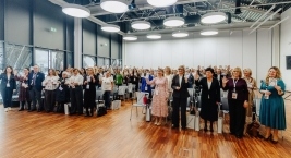 Uśmiechnięci uczestnicy konferencji stoją z wyciągniętymi dłońmi na których narysowana jest uśmiechnięta buźka, symbol Światowego Dnia Adopcji, niektórzy uczestnicy trzymają w dłoni obrazek z narysowaną uśmiechniętą buzią