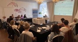 Osoby w sali konferencyjnej siedzą przy stołach, patrząc na prezentację na rzutniku