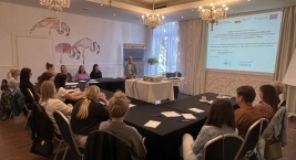 Uczestnicy spotkania siedzą przy stole, patrząc na osobę prezentującą treści na ekranie w sali